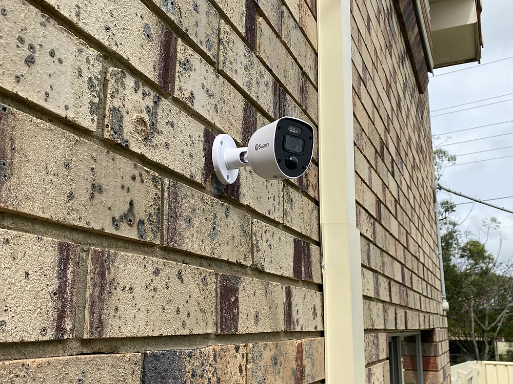 A white CCTV bullet camera mounted on a brick wall