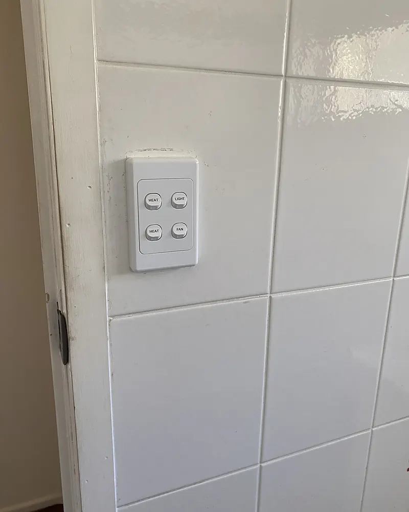 A four gang light switch plate on a white tiled wall